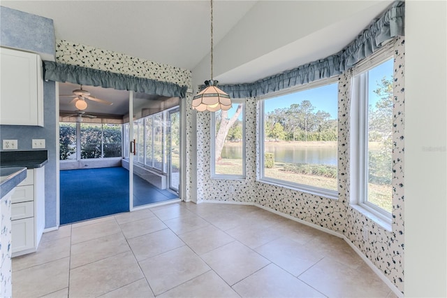 unfurnished dining area featuring a water view, light tile patterned floors, vaulted ceiling, and plenty of natural light