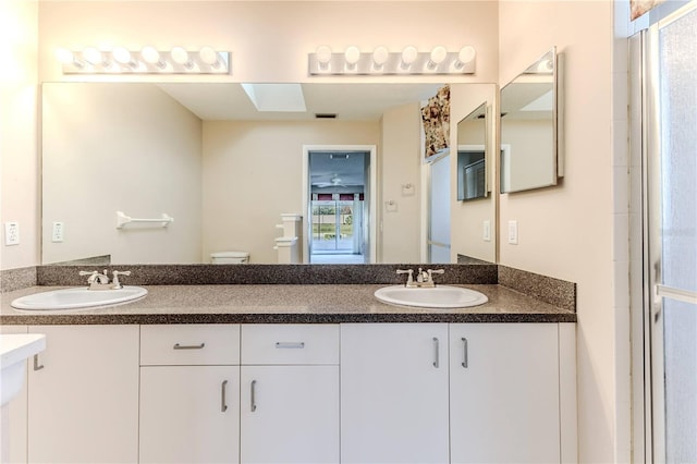 bathroom featuring a shower with shower door, toilet, vanity, and a skylight