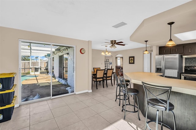 kitchen featuring appliances with stainless steel finishes, hanging light fixtures, light tile patterned floors, ceiling fan, and dark brown cabinetry