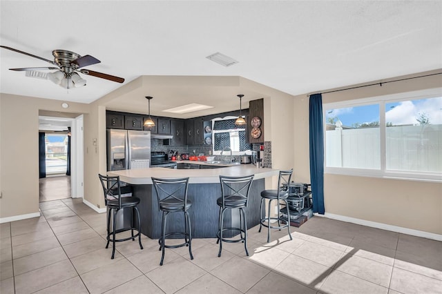 kitchen featuring stainless steel appliances, light tile patterned floors, kitchen peninsula, decorative backsplash, and a breakfast bar