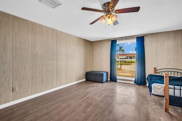 unfurnished bedroom featuring wood-type flooring, wooden walls, and ceiling fan