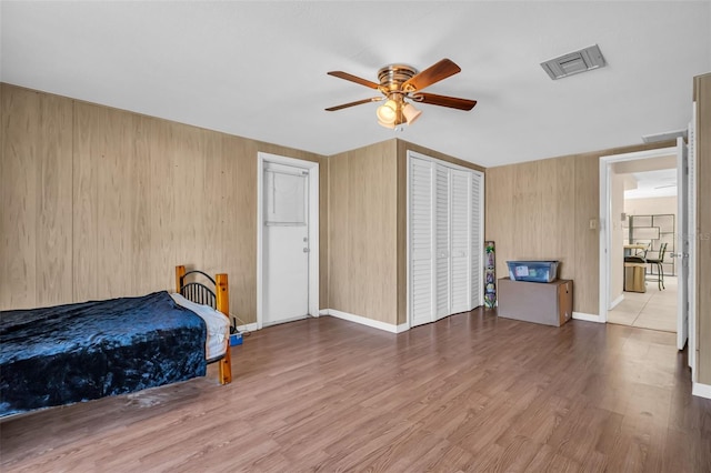 bedroom with a closet, hardwood / wood-style floors, wood walls, and ceiling fan