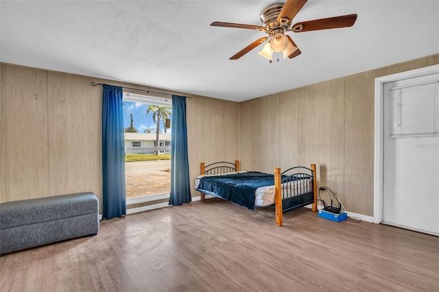 bedroom featuring light wood-type flooring, wood walls, and ceiling fan