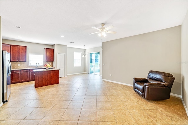 kitchen featuring a kitchen island, stainless steel refrigerator, backsplash, light tile patterned flooring, and ceiling fan