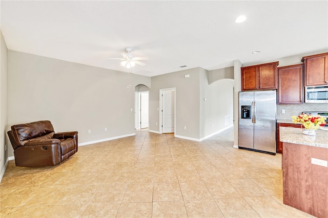 kitchen featuring light stone countertops, stainless steel appliances, decorative backsplash, ceiling fan, and light tile patterned floors