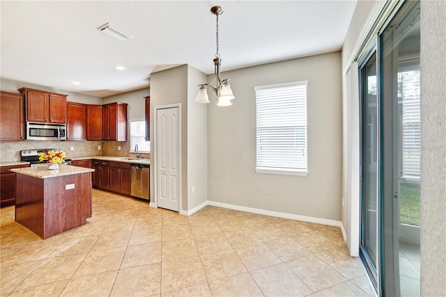 kitchen featuring appliances with stainless steel finishes, a center island, a notable chandelier, decorative light fixtures, and sink