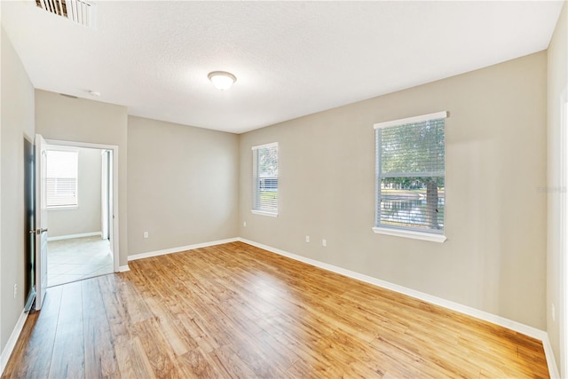 empty room featuring plenty of natural light, a textured ceiling, and light hardwood / wood-style flooring