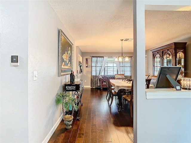 dining area featuring dark wood-type flooring, a textured ceiling, and a chandelier