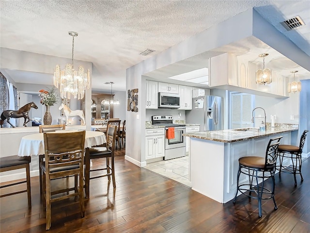 kitchen with white cabinets, appliances with stainless steel finishes, sink, stone countertops, and kitchen peninsula