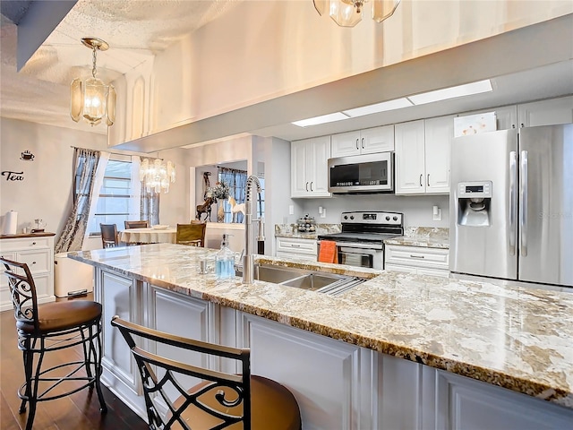 kitchen with white cabinetry, appliances with stainless steel finishes, a kitchen breakfast bar, hanging light fixtures, and light stone countertops