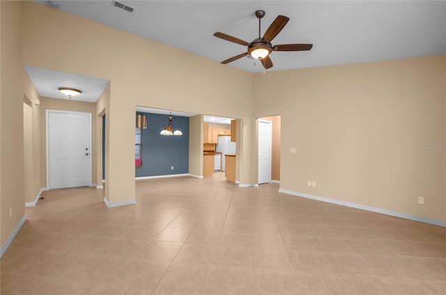 unfurnished living room with ceiling fan with notable chandelier, a towering ceiling, and light tile patterned flooring