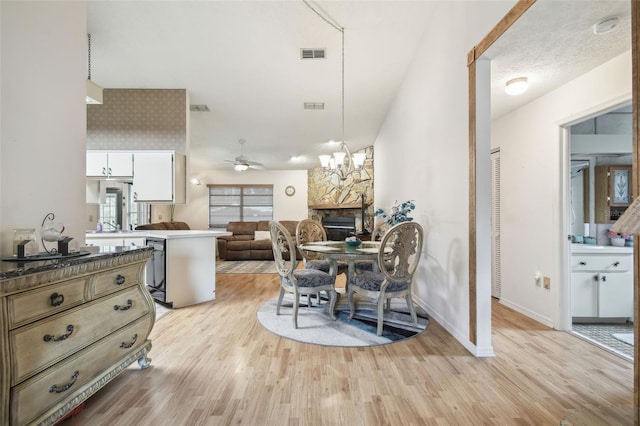 dining space featuring a stone fireplace, a textured ceiling, ceiling fan with notable chandelier, light hardwood / wood-style flooring, and sink