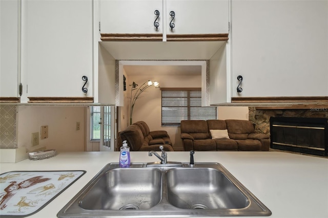 kitchen with backsplash, a fireplace, sink, and white cabinetry