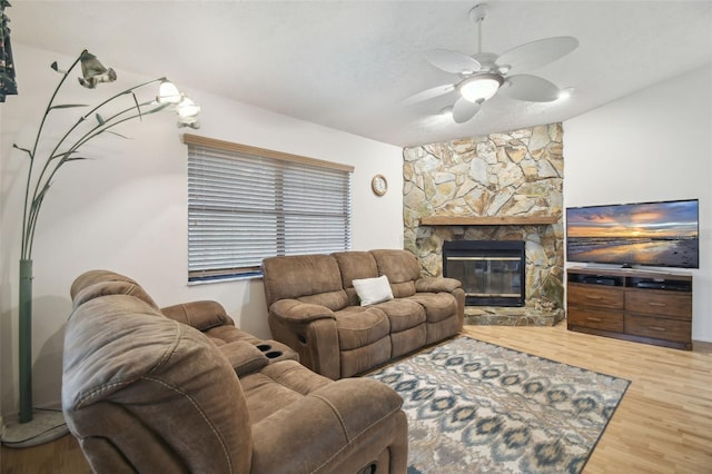 living room featuring a textured ceiling, ceiling fan, wood-type flooring, and a stone fireplace