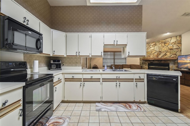 kitchen featuring a stone fireplace, sink, white cabinetry, kitchen peninsula, and black appliances