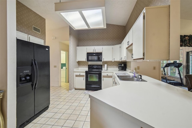 kitchen featuring sink, white cabinets, light tile patterned floors, black appliances, and washing machine and dryer