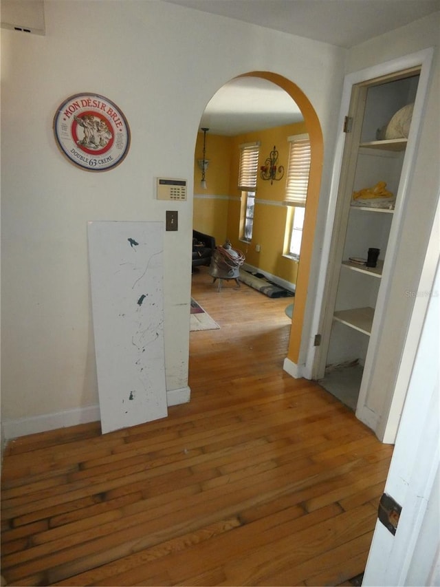 corridor with arched walkways, baseboards, and wood-type flooring