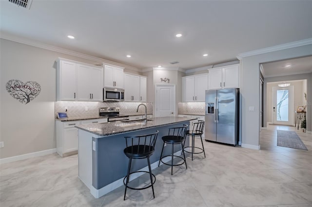 kitchen with sink, dark stone countertops, white cabinetry, stainless steel appliances, and a center island with sink