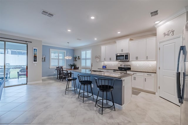 kitchen with appliances with stainless steel finishes, an island with sink, dark stone counters, and white cabinets