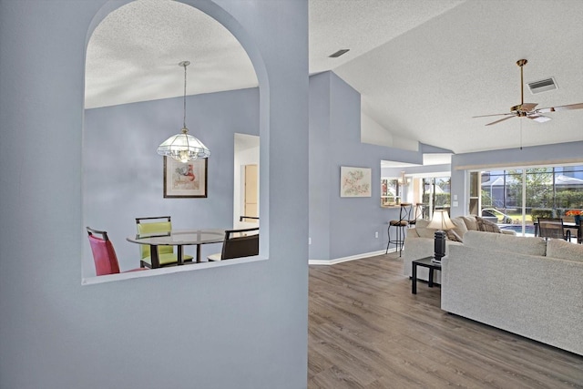 living room featuring lofted ceiling, ceiling fan with notable chandelier, a textured ceiling, and hardwood / wood-style flooring