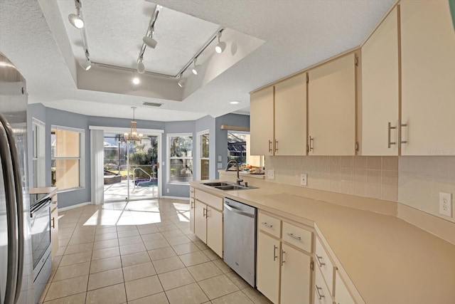 kitchen featuring sink, appliances with stainless steel finishes, a tray ceiling, pendant lighting, and cream cabinets