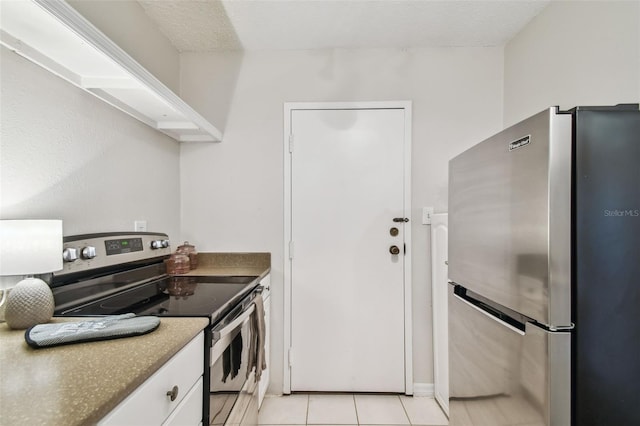 kitchen with white cabinets, light tile patterned floors, stainless steel appliances, and a textured ceiling