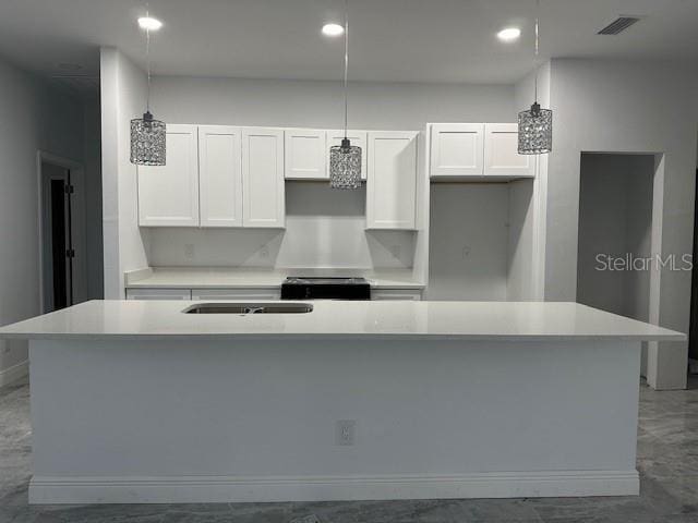 kitchen with a kitchen island with sink, white cabinetry, and pendant lighting