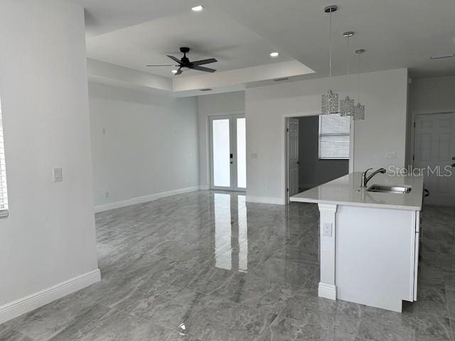 kitchen featuring decorative light fixtures, ceiling fan, a raised ceiling, sink, and a kitchen island with sink