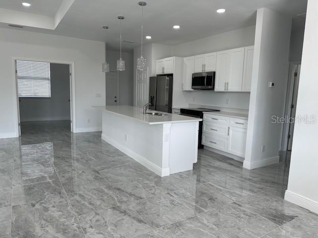 kitchen featuring an island with sink, white cabinetry, hanging light fixtures, stainless steel appliances, and sink