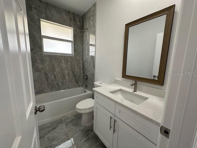 full bathroom featuring vanity, tiled shower / bath, and toilet