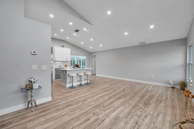 interior space featuring vaulted ceiling, a kitchen island, white cabinetry, light wood-type flooring, and a kitchen breakfast bar