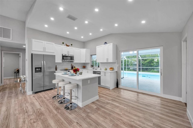 kitchen with backsplash, white cabinetry, stainless steel appliances, and a kitchen island