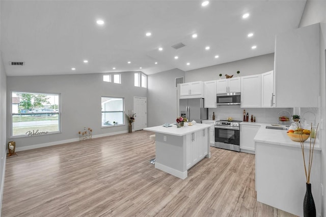 kitchen with stainless steel appliances, a center island, white cabinets, light hardwood / wood-style flooring, and sink