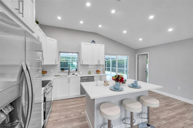 kitchen featuring white cabinetry, stainless steel appliances, a healthy amount of sunlight, vaulted ceiling, and a center island