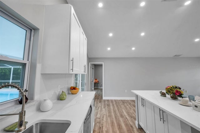 kitchen with light stone countertops, white cabinets, dishwasher, sink, and light hardwood / wood-style flooring