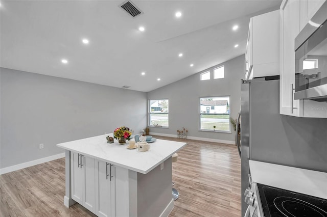 kitchen featuring stainless steel appliances, lofted ceiling, white cabinets, light hardwood / wood-style flooring, and a center island