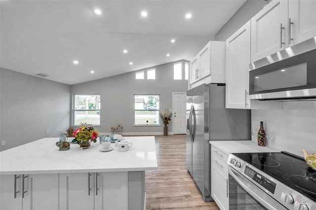 kitchen featuring appliances with stainless steel finishes, a center island, lofted ceiling, white cabinetry, and light stone counters