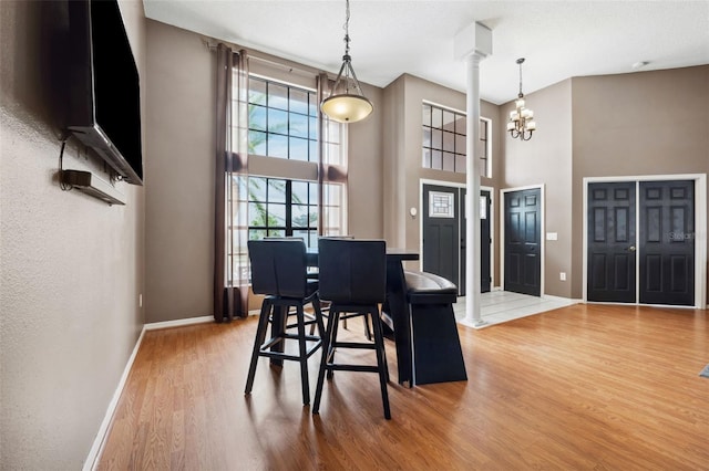 dining room with hardwood / wood-style floors, a towering ceiling, a chandelier, and ornate columns