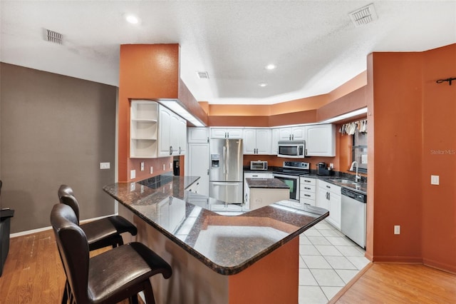 kitchen featuring kitchen peninsula, sink, appliances with stainless steel finishes, a textured ceiling, and white cabinets