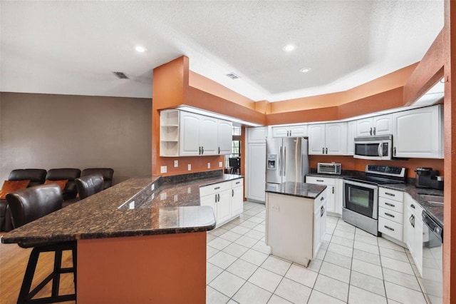 kitchen with a textured ceiling, white cabinets, a kitchen island, stainless steel appliances, and kitchen peninsula