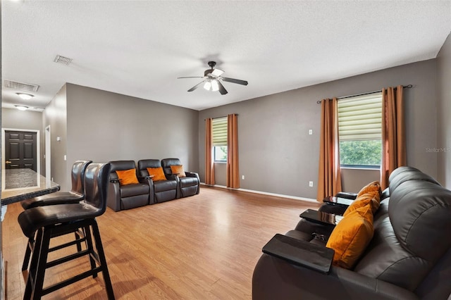 living room with light wood-type flooring, ceiling fan, and a textured ceiling