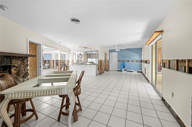 tiled dining area with ceiling fan and a stone fireplace