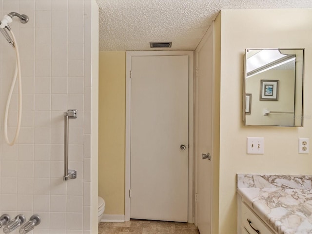 bathroom featuring vanity, a tile shower, a textured ceiling, and toilet