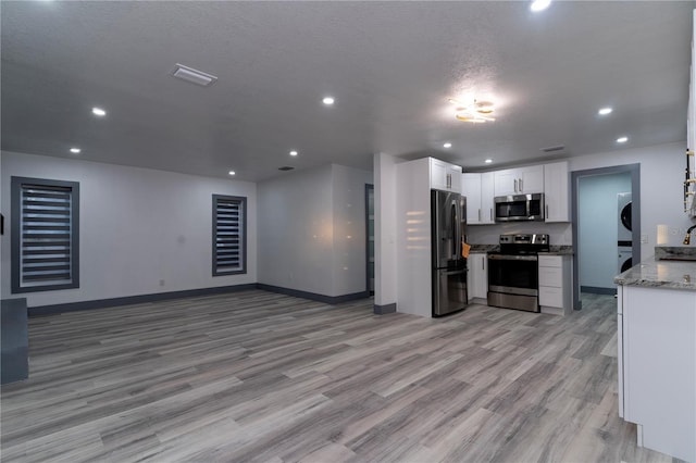 kitchen featuring stainless steel appliances, light wood-type flooring, stacked washing maching and dryer, white cabinets, and light stone counters