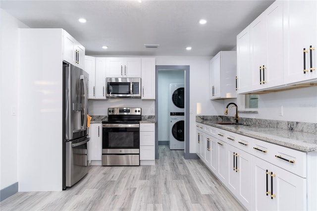 kitchen with stacked washer and dryer, appliances with stainless steel finishes, white cabinets, light stone counters, and sink