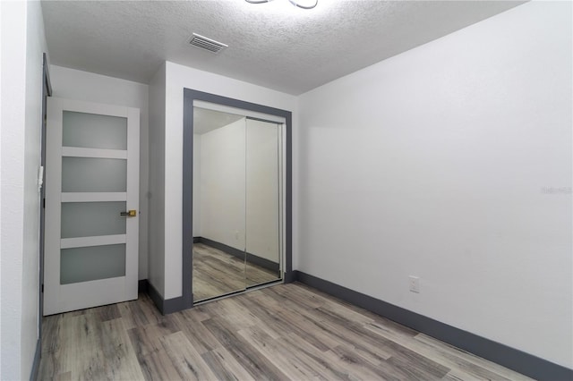 unfurnished bedroom featuring hardwood / wood-style flooring, a textured ceiling, and a closet