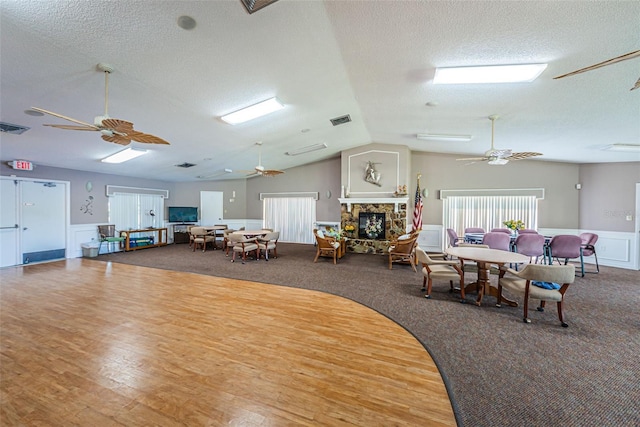 dining room featuring ceiling fan, a stone fireplace, vaulted ceiling, and a textured ceiling