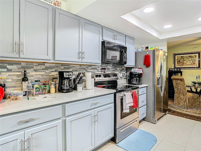 kitchen with backsplash, a tray ceiling, gray cabinets, light tile patterned flooring, and stainless steel appliances