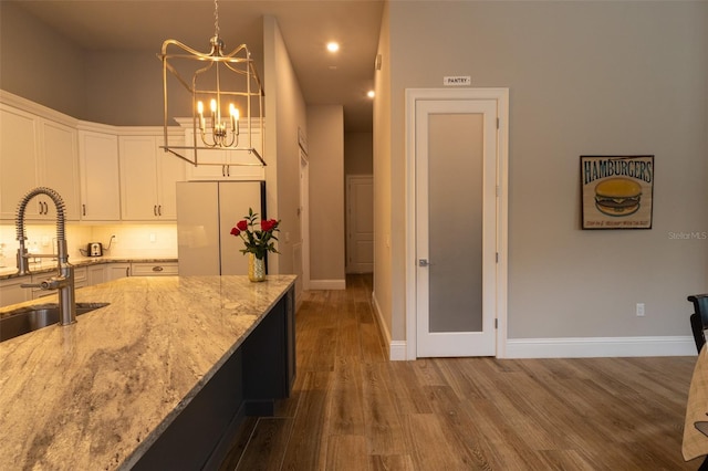 kitchen with light stone countertops, white fridge, white cabinets, decorative light fixtures, and sink