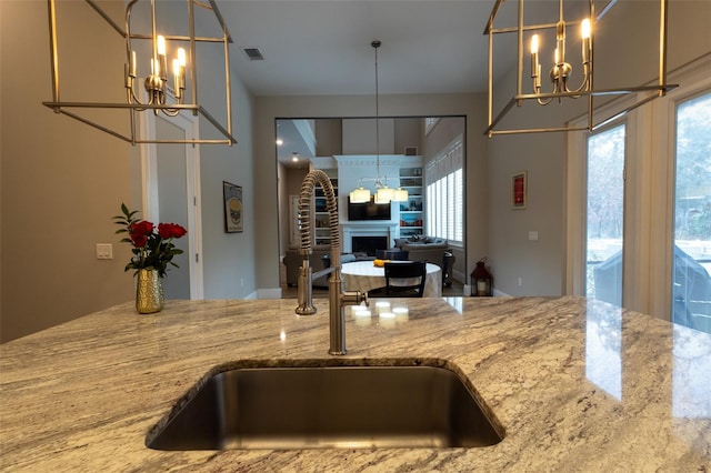 kitchen featuring sink, an inviting chandelier, pendant lighting, and stone counters